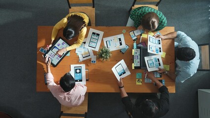 Top view of project manager discussing about Ux Ui design for mobile phone interface. Start team brainstorm about wireframe prototype design while looking at tablet at Creative workplace. Convocation.