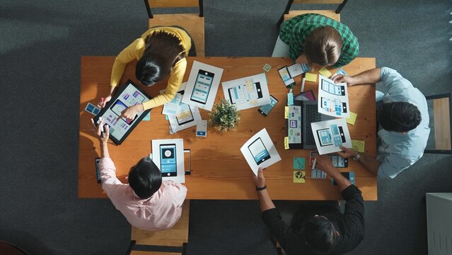 Top view of project manager discussing about Ux Ui design for mobile phone interface. Start team brainstorm about wireframe prototype design while looking at tablet at Creative workplace. Convocation.