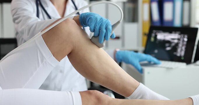 Woman doctor in gloves presses ultrasound probe to patient leg. Vascular specialist scans blood flow on monitor checking vein health at appointment