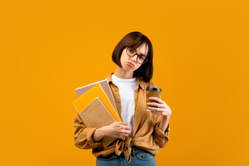 Obraz premium So tired. Exhausted female student with notebooks and takeaway coffee looking at camera on yellow studio background. Lady fatigue from preparing for college or university exams
