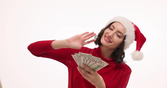 Happy woman in Santa hat fans stack of banknotes sliding with joy. Festive earner counts holiday bonus cash dreaming about future shopping slow motion