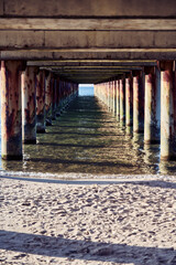 Fototapeta premium Rusted pier structure over Baltic Sea waters with Sandy Beach foreground