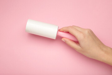 Woman holding lint roller on pink background.