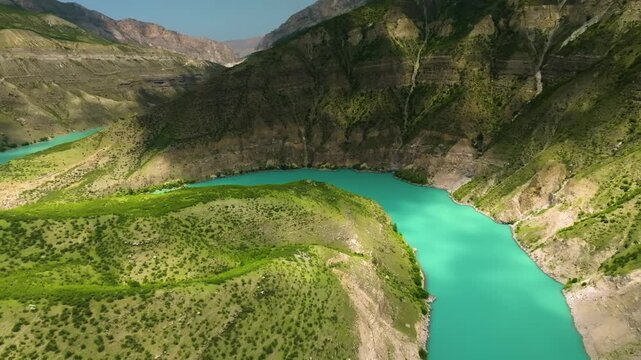 drone footage captures the landscape of the Sulak Canyon in Dagestan, Russia. The video shows the vibrant turquoise Sulak River winding through the deep gorge of the Caucasus Mountains on a sunny summ
