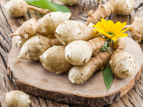 Freshly harvested Jerusalem artichoke (sunchoke) tubers with a yellow flower and green leaves, arranged on a rustic wooden table.