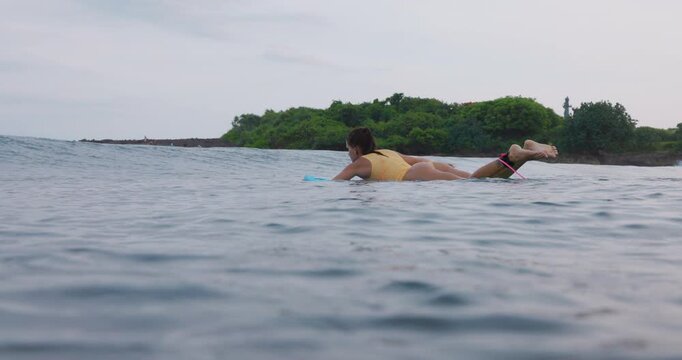 Young surfer woman with perfect body on surfboard in ocean with waves.
