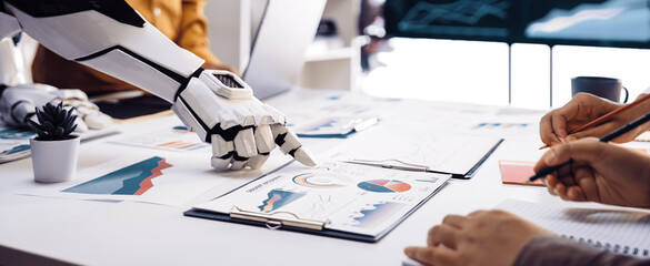A robot collaborates with a human in a modern office showcasing various charts and graphs on a table, illustrating technology's role in data-driven decision making.Noogenesis