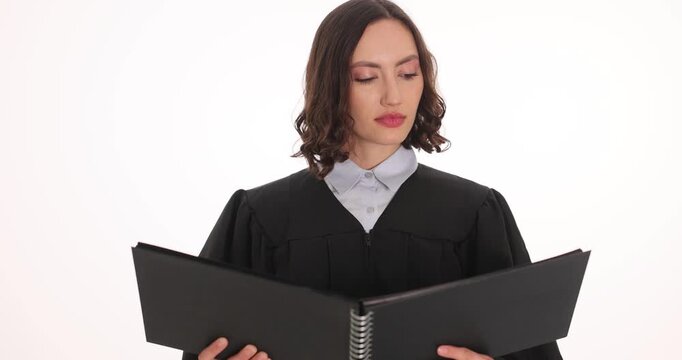 Woman judge in black robe holds folder while reading case file. Serious magistrate studies document pages preparing important verdict slow motion