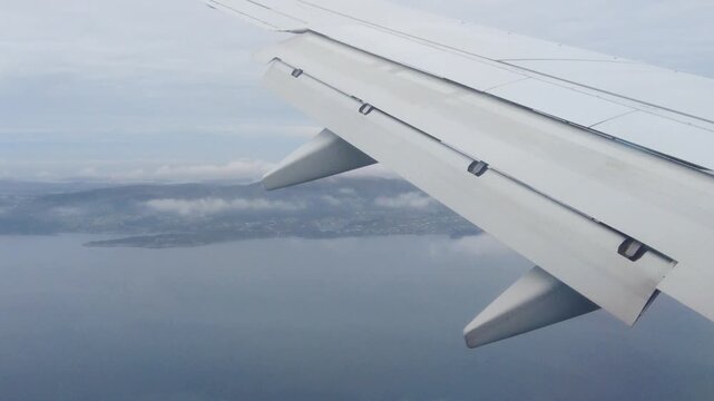 white wing deployed flaps extends hazy coastal landscape dark islands calm water partially obscured by low lying clouds norway airplane low-lying aviation transport travel aerospace landing 