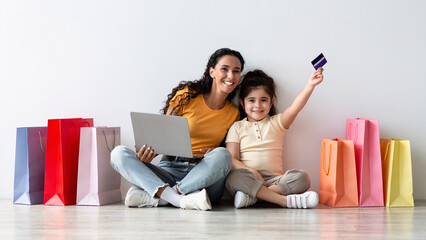 Online Shopping Concept. Happy middle eastern mother and little daughter sitting on floor with...