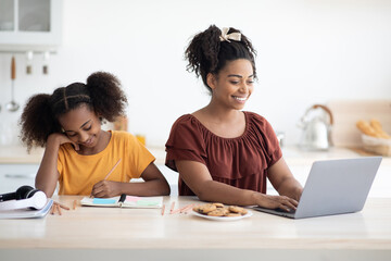 Happy african american school girl teenager doing homework, sitting at table by her cheerful...