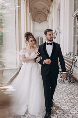 Fototapeta premium Couple walks together at a wedding venue near elegant architecture in daylight