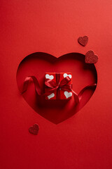 A vertical red Valentine scene features a heart cutout, a gift box with white hearts, ribbon, and...