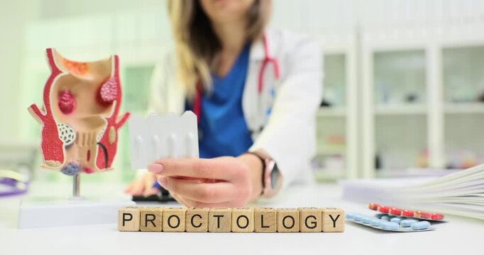 Wooden cubes spell word Proctology near rectum model. Woman doctor holds blister pack explaining bowel disease treatment clearly for patient in clinic