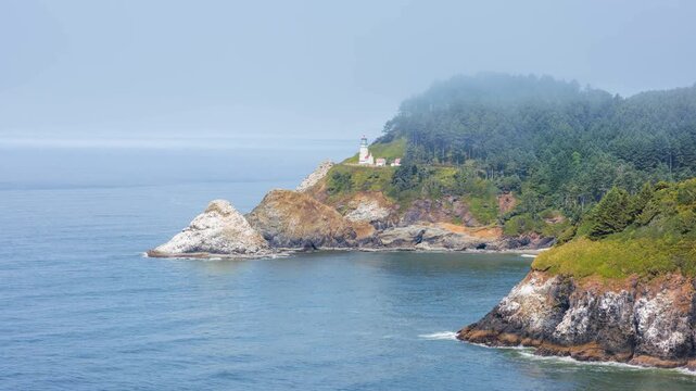 A scenic view of the historic Heceta Head Lighthouse and the rugged Oregon coastline on a foggy day. The lighthouse, built in 1894, stands 205 feet above the Pacific Ocean and is a working beacon list