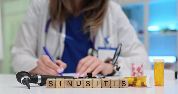 Wooden cubes spell word Sinusitis near otoscope and yellow pill vial. Woman doctor writes prescription tracking progress of chronic sinus pain