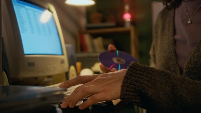 Close-up of hands of anonymous young woman searching through stack of cd disks, while looking to install software or record files, while working on old personal computer at home