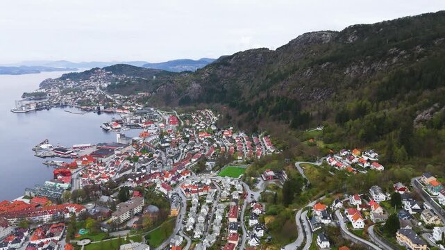 coastal city densely packed white houses red roofs town tucked between rocky slopes forested mountain vast northern fjord norway bergen center port settlement urban landscape 