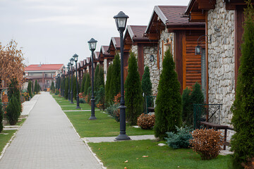 Row of wooden houses with stone walls and green trees along a pathway in a quiet neighborhood in autumn