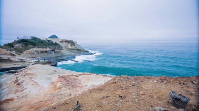 High-angle scenic view of rugged coastal landforms at Cape Kiwanda State Natural Area in Pacific City, Oregon. Powerful ocean waves break against the base of the large, unique sandstone headland under