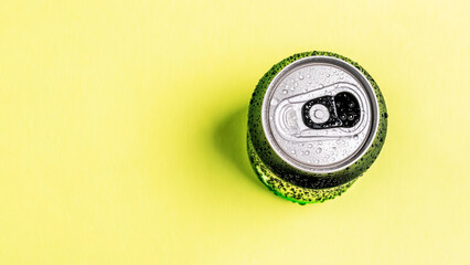 Single green aluminum can covered in water droplets on a vibrant yellow surface, presenting a cool and refreshing drink