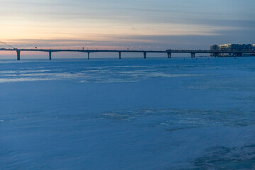 Panoramic view of the Western High-Speed Diameter bridge spanning across the frozen Gulf of Finland during winter at dusk with golden sunset light on the ice surface.