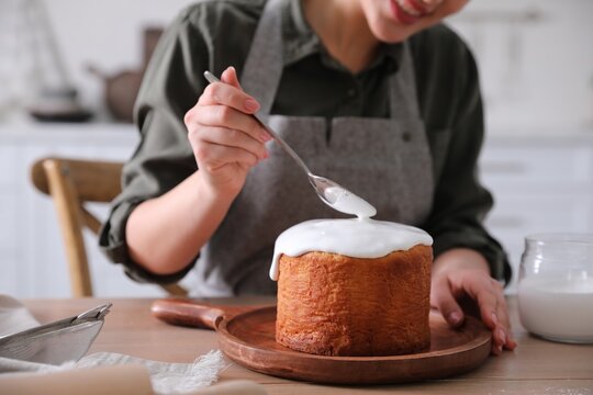 Young woman decorating traditional Easter cake with glaze in kitchen, closeup