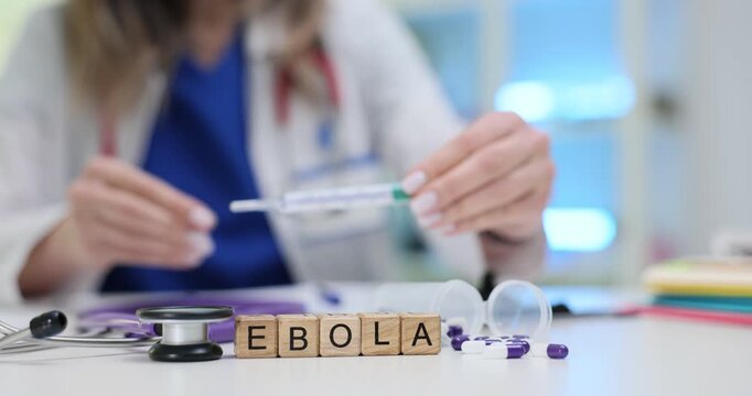 Woman doctor shows thermometer during consultation at appointment. Miniature wooden cubes form word Ebola on table indicating diagnosis of patient