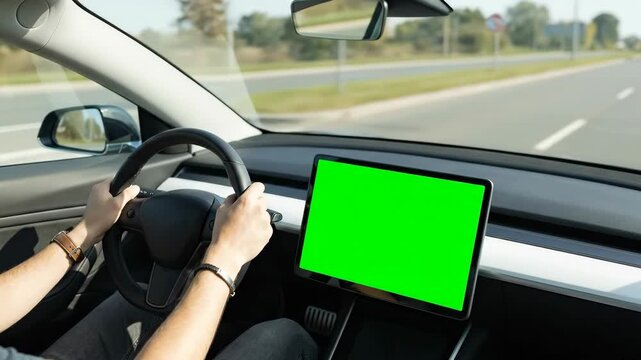 A driver holds the steering wheel while a car drives on a highway with a green screen dashboard display. Concept of automotive technology and navigation.