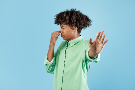 Terrible smell. African american guy closing his nose and gesturing STOP, feeling disgusted, standing on blue studio background. Black male repulsed by unpleasant odor or stinky perfume
