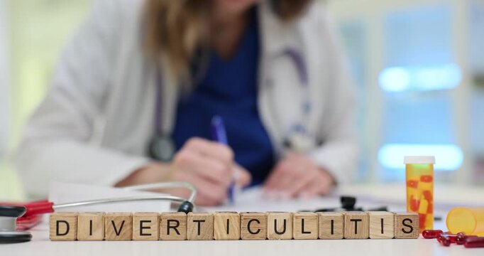 Doctor carefully prescribes tablets focusing on reducing symptoms. Wooden cubes form word Diverticulitis on table near stethoscope and medication