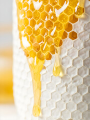 Golden organic honey dripping down a white textured honeycomb, fresh natural nectar for food industry branding and healthy lifestyle concepts.
