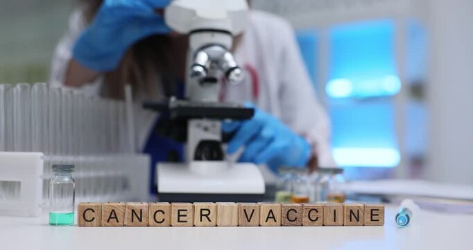 Text Cancer Vaccine on wooden blocks with vial and syringe in medical lab. Female scientist looks in microscope analyzing tissue after treatment
