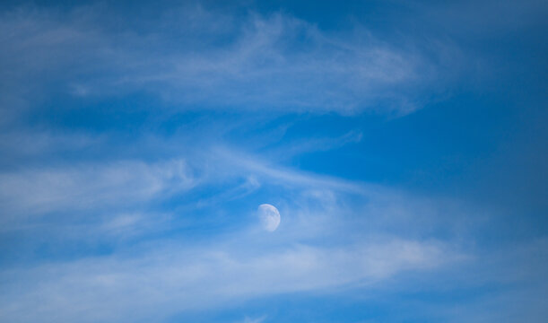 the moon in broad daylight behind the clouds