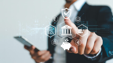 Businessman interacting with digital security icons in futuristic interface with shield and bank symbols in blue glowing light for financial technology