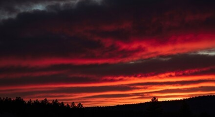 Obraz premium Fiery sunset paints the sky with red and orange stripes over a dark silhouetted landscape