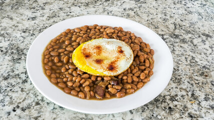 Plate of beans with a fried egg served on a white plate on a granite table