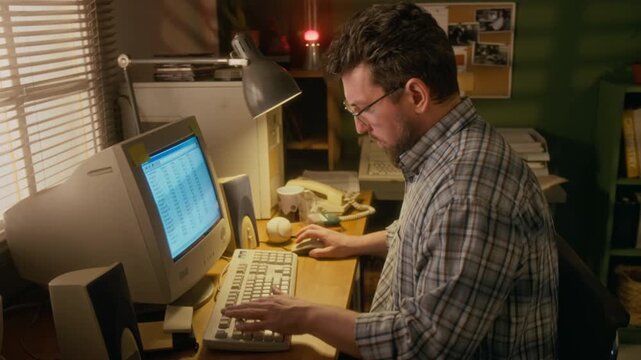 Medium side shot of busy middle-aged Caucasian man working on financial report in spreadsheet program on vintage desktop computer with CRT monitor at home office, using keyboard and wired mouse
