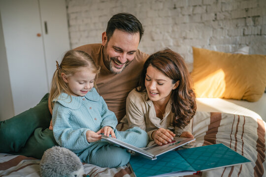 Parents and daughter reading a book in bed enjoying family time