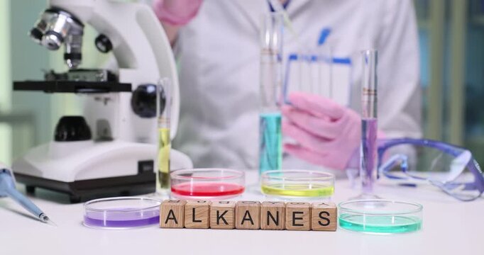 Researcher carefully adds liquid reagent into test tubes using pipette. Wooden cubes form word Alkanes clearly identifying chemical group under study