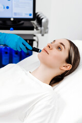 Fototapeta premium Female cosmetologist performing hydrafacial treatment on a patient lying on a treatment bed with a skincare device and monitor in a bright, modern beauty clinic setting