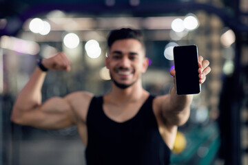Fitness App. Sporty Muscular Arab Man Holding Smartphone With Blank Black Screen And Showing Biceps...