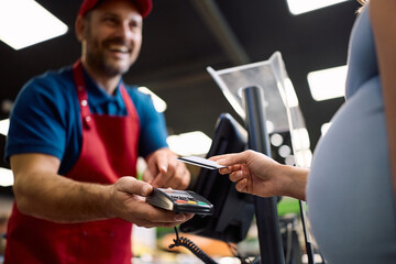 Close up of pregnant woman using credit car while paying bill at cash register.