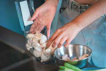 Hands of a young woman taking fresh mushrooms out of a box and placing them in a casserole dish.