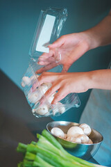Hands of a young woman taking fresh mushrooms out of a box and placing them in a casserole dish.