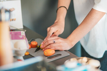 Close-up of a young woman's hands cutting bell peppers on a cutting board in her kitchen at home.