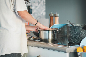 Hands of a young woman serving vegetables into a pot to boil them on the electric stove, cooking at home,