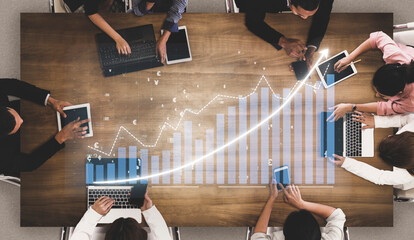 A top-down view of a business meeting showcasing diverse professionals analyzing data on devices, with graphs indicating growth and collaborative effort. Impute