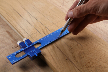 A silver pencil marks lines on a wooden board alongside a blue metal Procision gauge, showcasing the intersection of technical measurement and manual woodworking skill.