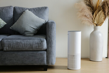 A sleek white air purifier placed beside a sofa in a modern living room, creating a clean, calm, and healthy indoor environment. The minimalist design blends seamlessly with contemporary home decor, h